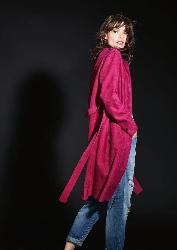 Eine Frau trägt einen lila Mantel und Jeans.