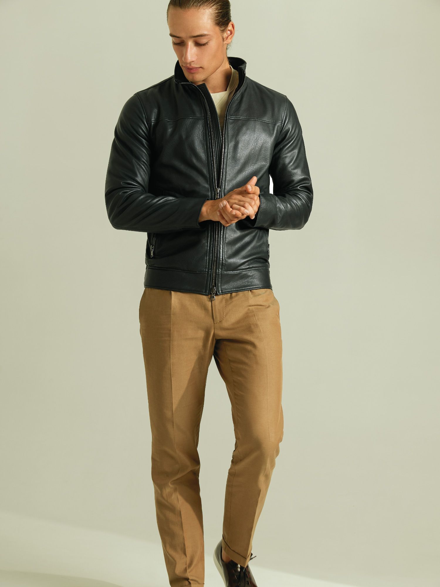 Ein Mann trägt eine schwarze Lederjacke und braune Hosen.