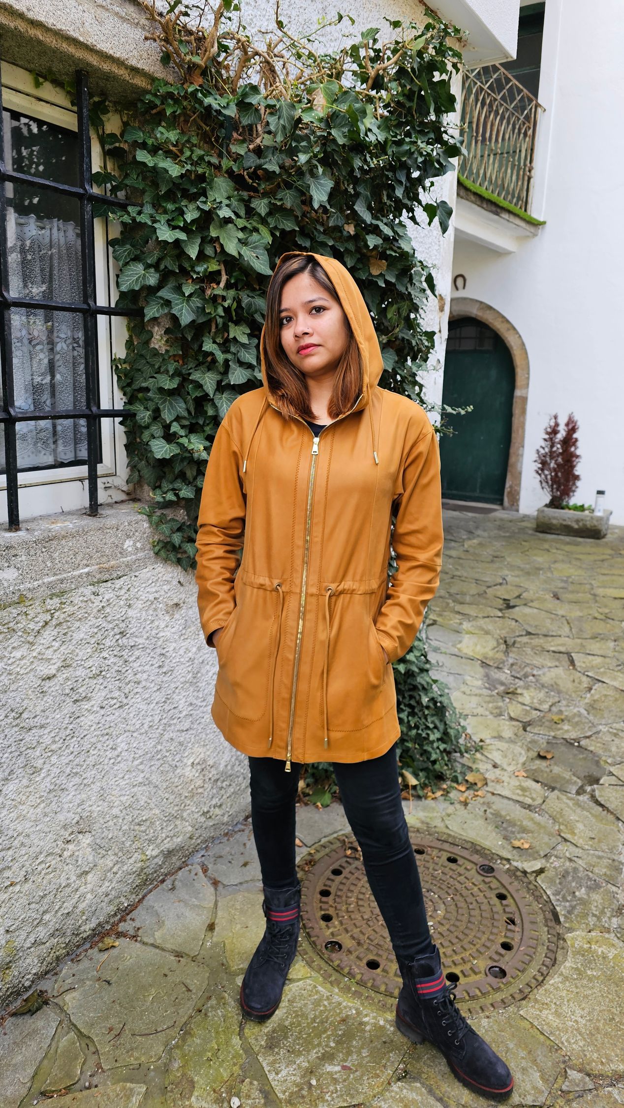 Eine Frau in einem gelben Mantel mit Kapuze steht vor einem Gebäude.