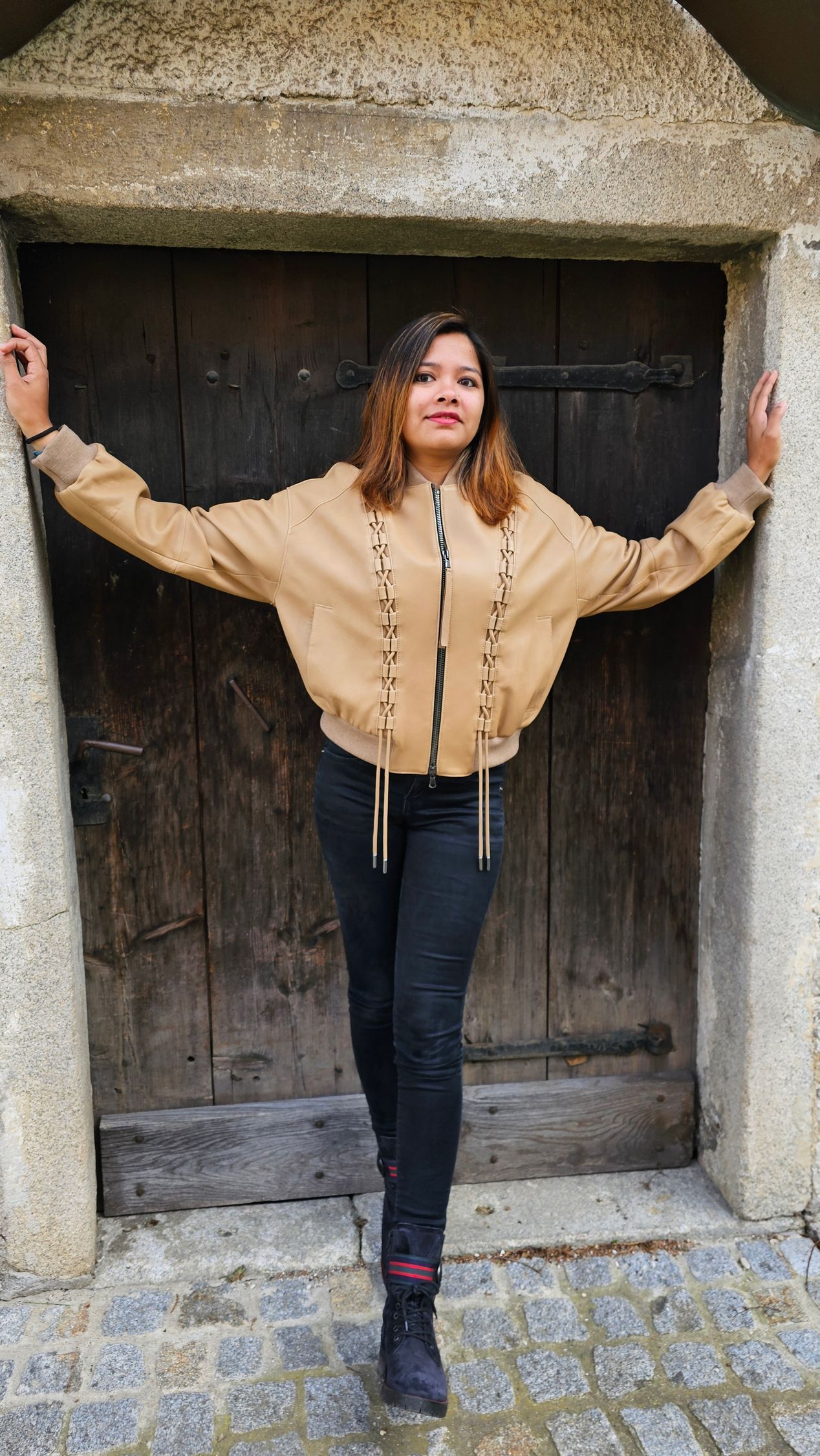 Eine Frau steht mit ausgestreckten Armen vor einer Holztür.