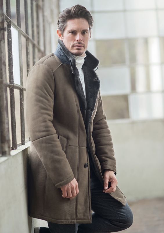 Ein Mann in einem braunen Mantel lehnt an einer Wand.