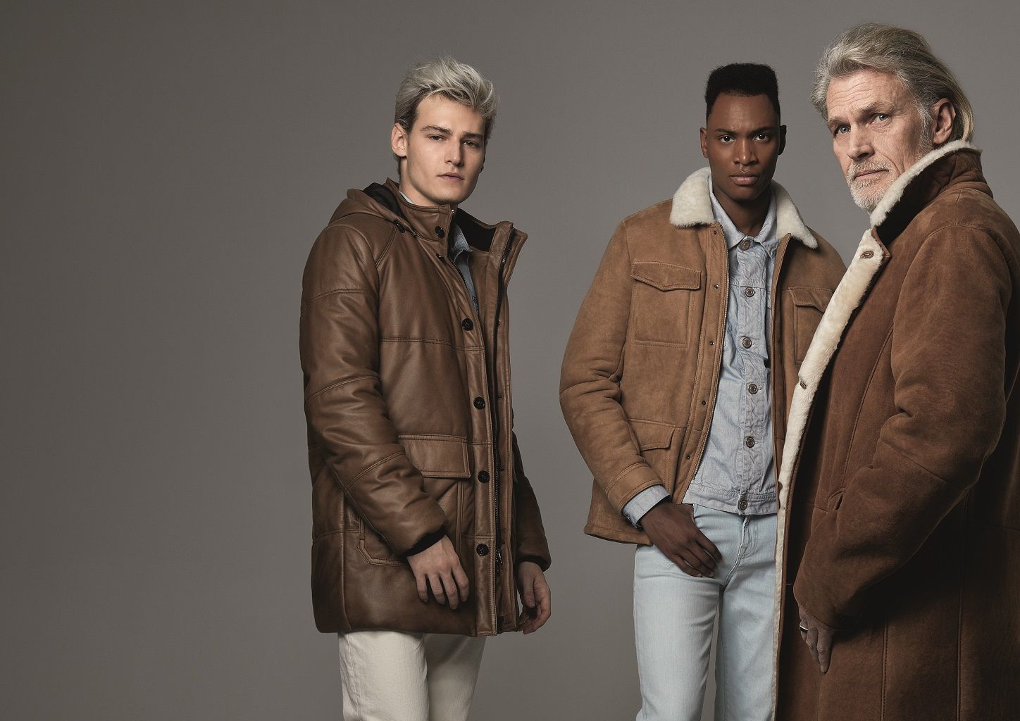 Drei Männer in braunen Mänteln stehen nebeneinander.