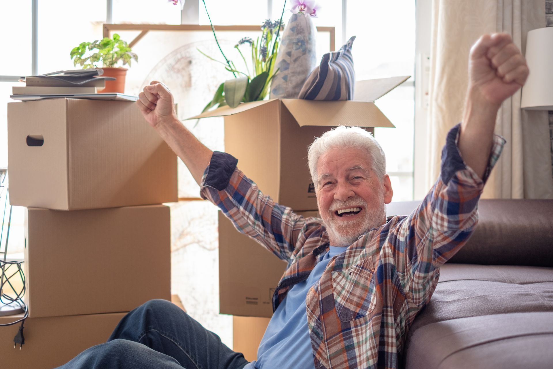 Ein älterer Mann sitzt auf einem Sofa mit erhobenen Armen.