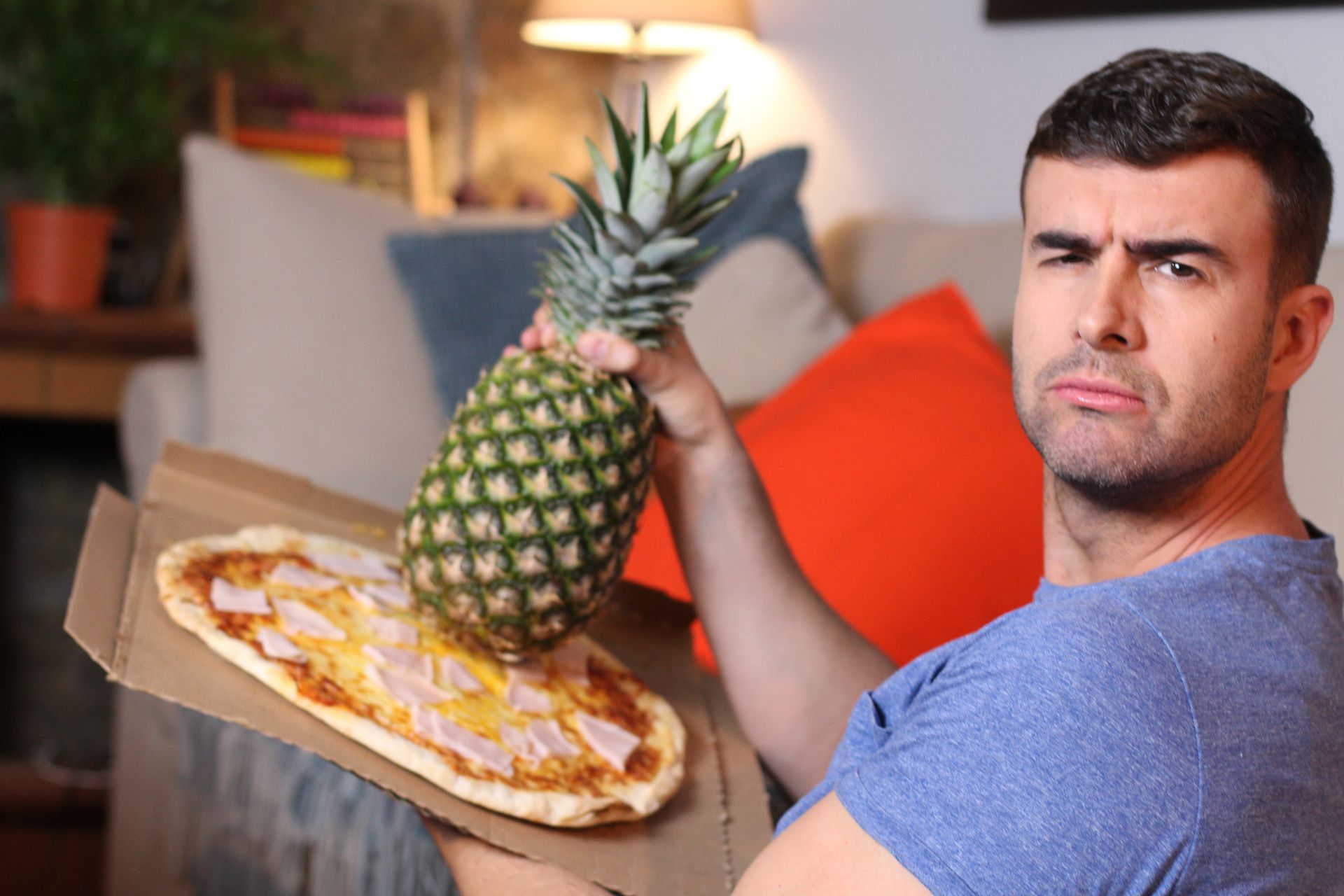 Homme faisant la grimace déposant un ananas sur une pizza jambon fromage tomate