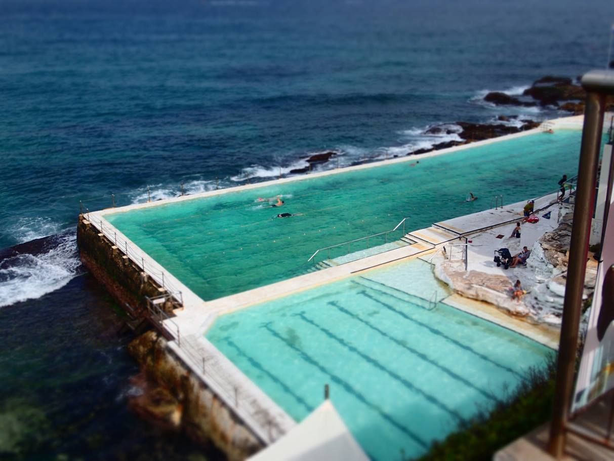Meerwasserbecken mit türkisfarbenem Wasser, Schwimmern und felsiger Küste.