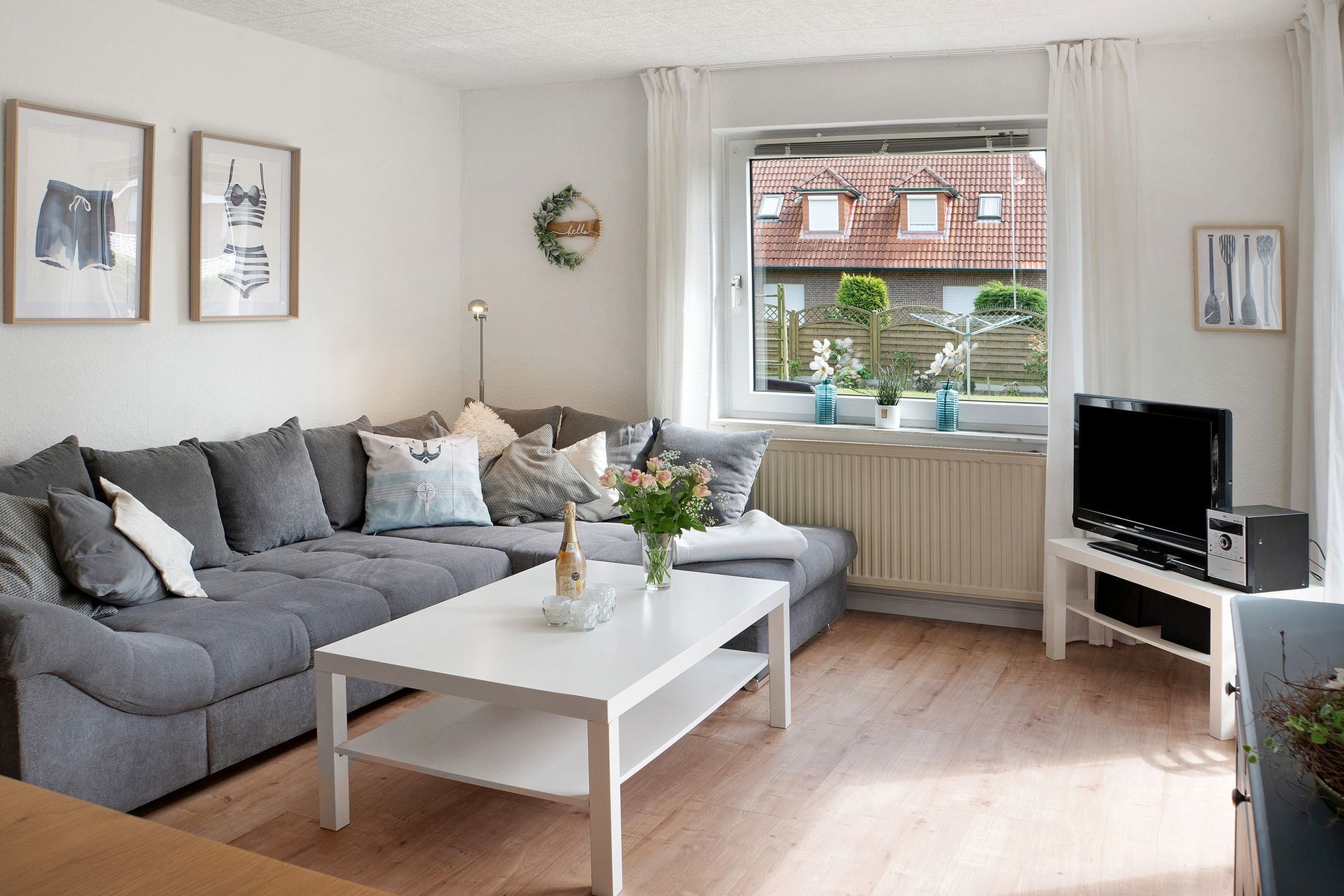 Gemütliches Wohnzimmer mit grauer Eckcouch, weißem Couchtisch und Fenster mit Blick über die Dächer.