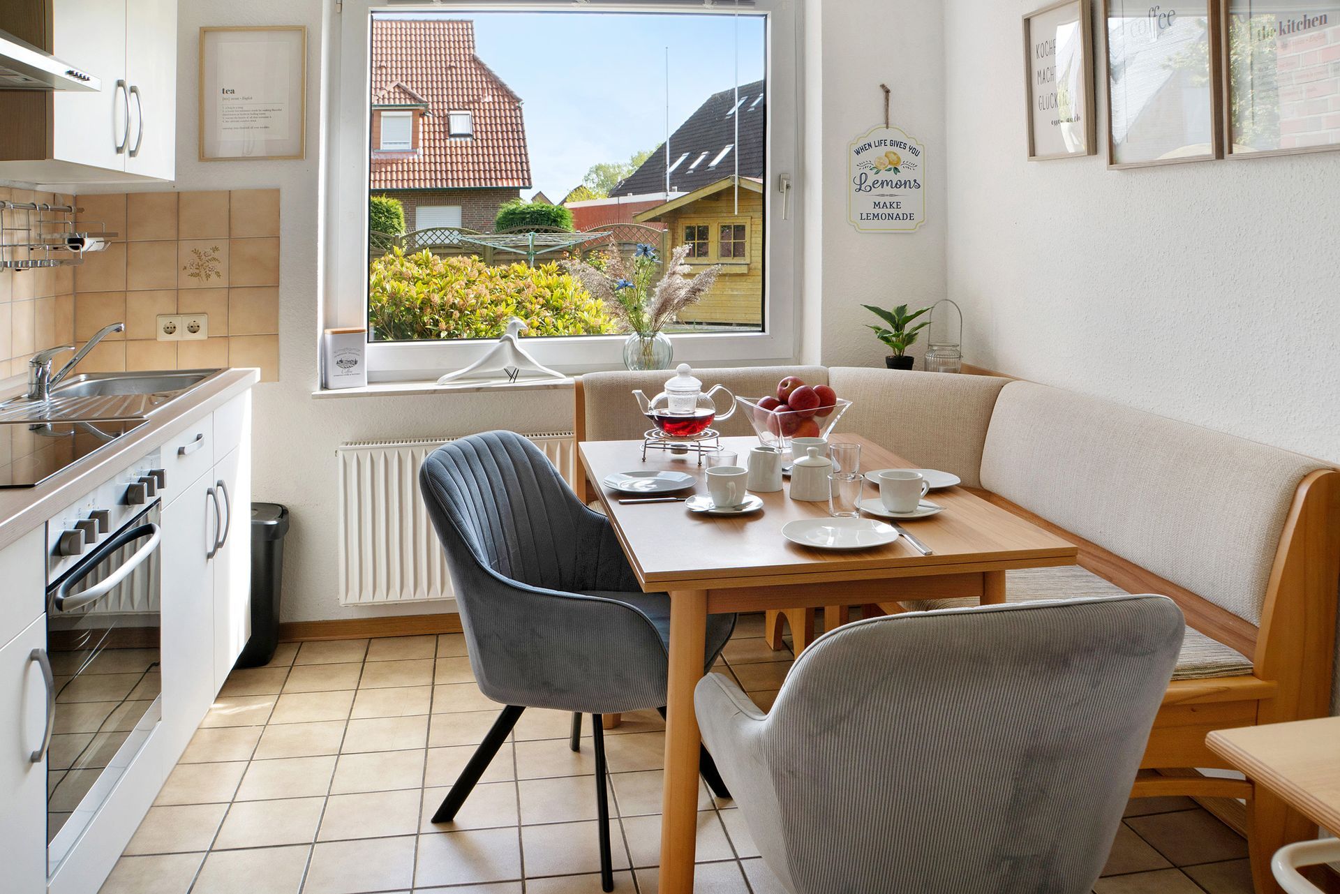 Kleine Küche mit gedecktem Tisch. Fenster mit Aussicht, weiße Küchengeräte, zwei Polsterstühle.