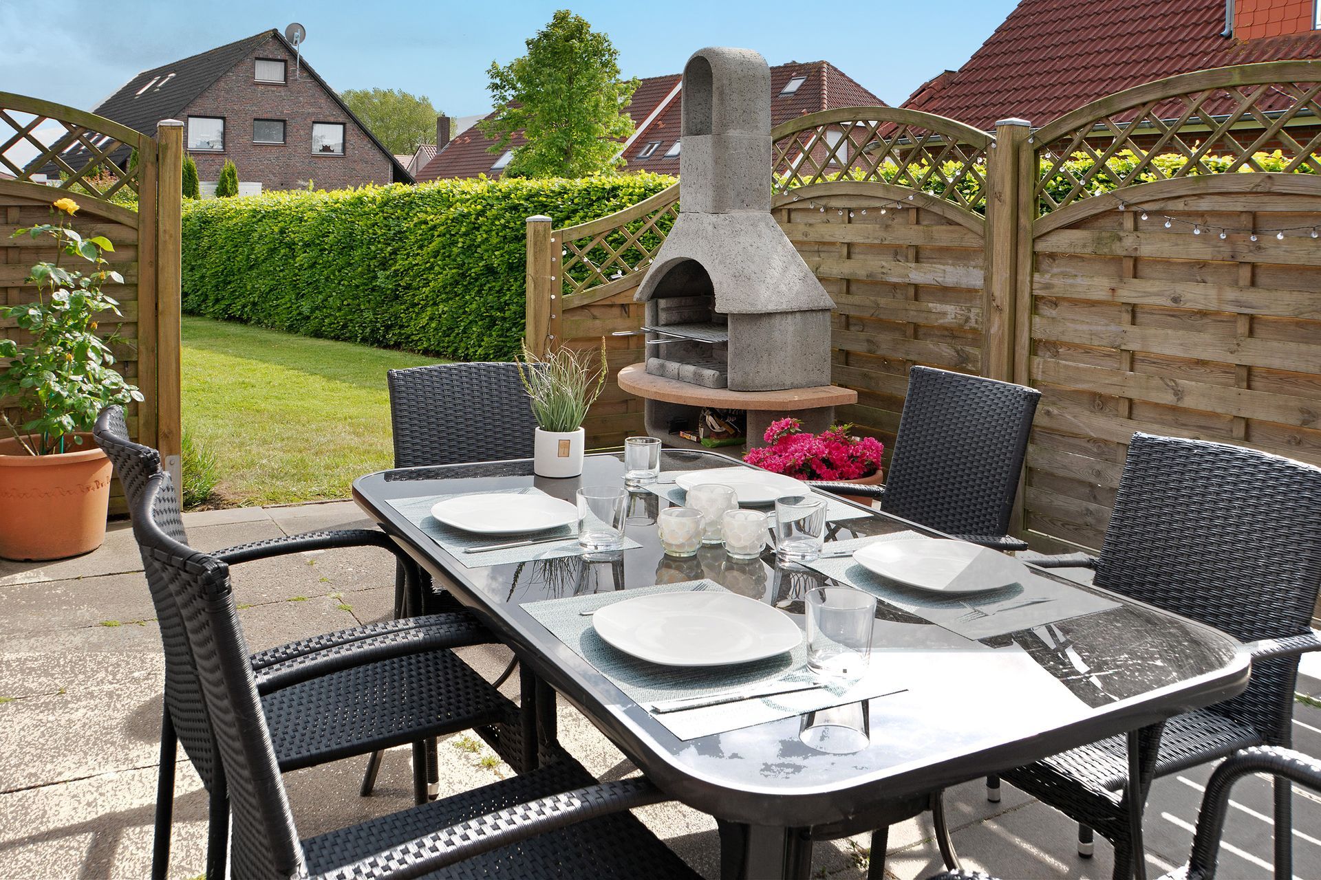 Terrasse mit gedecktem Esstisch, Außengrill und grünem Rasen im Hintergrund.