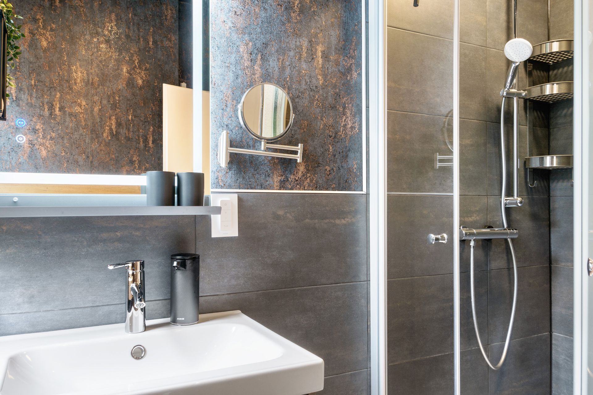 Modernes Badezimmer mit Waschbecken, Dusche und Spiegel vor einer dunklen, strukturierten Wand.