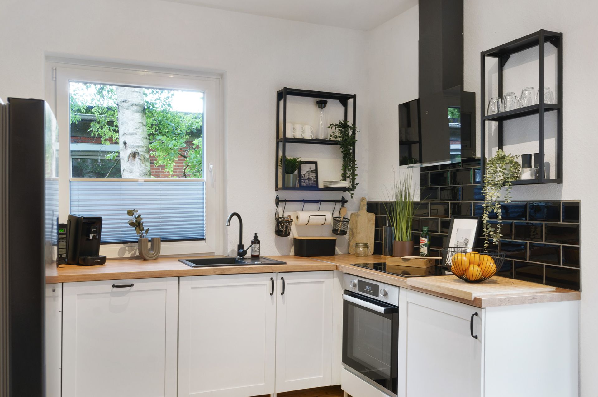 Weiße Küche mit schwarzen Akzenten, Arbeitsplatten aus Holz und einem Fenster mit Blick ins Grüne.