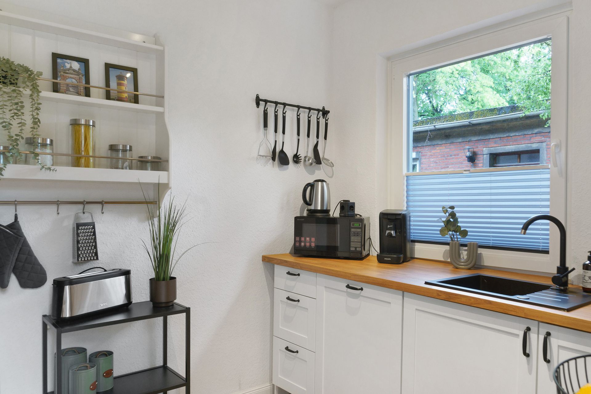 Eine kleine, weiße Küche mit Holzarbeitsplatte und Edelstahlgeräten. Ein Fenster bietet Blick ins Grüne.