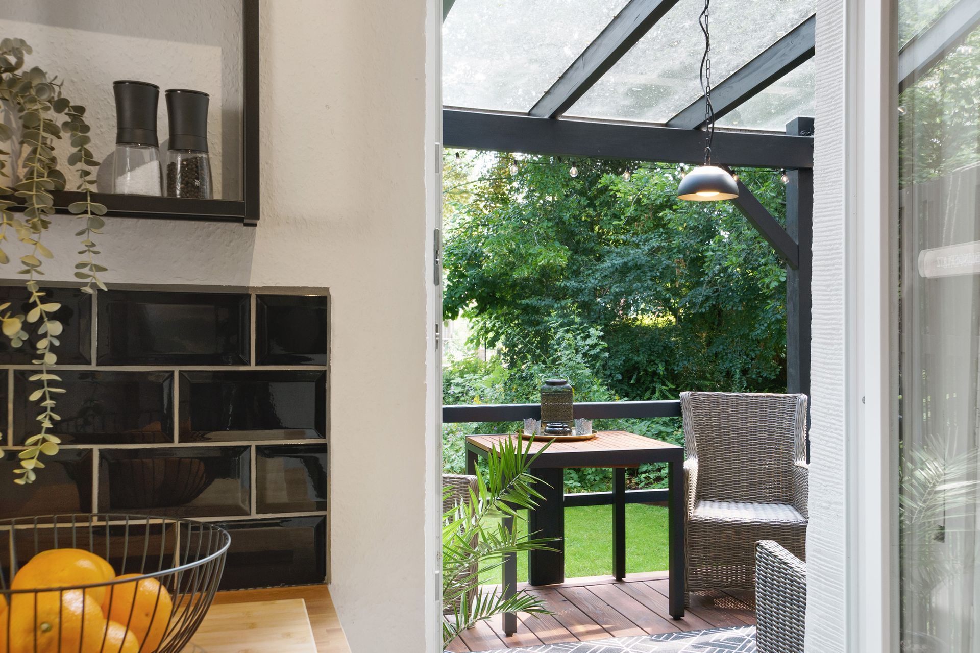 Terrasse mit Tisch, Stuhl und Hängelampe, vom Innenbereich aus betrachtet.