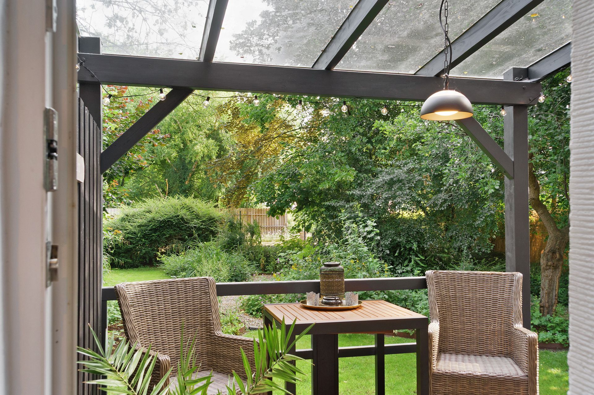 Terrasse mit Tisch und Stühlen unter einer Pergola mit Blick auf einen üppigen grünen Garten.