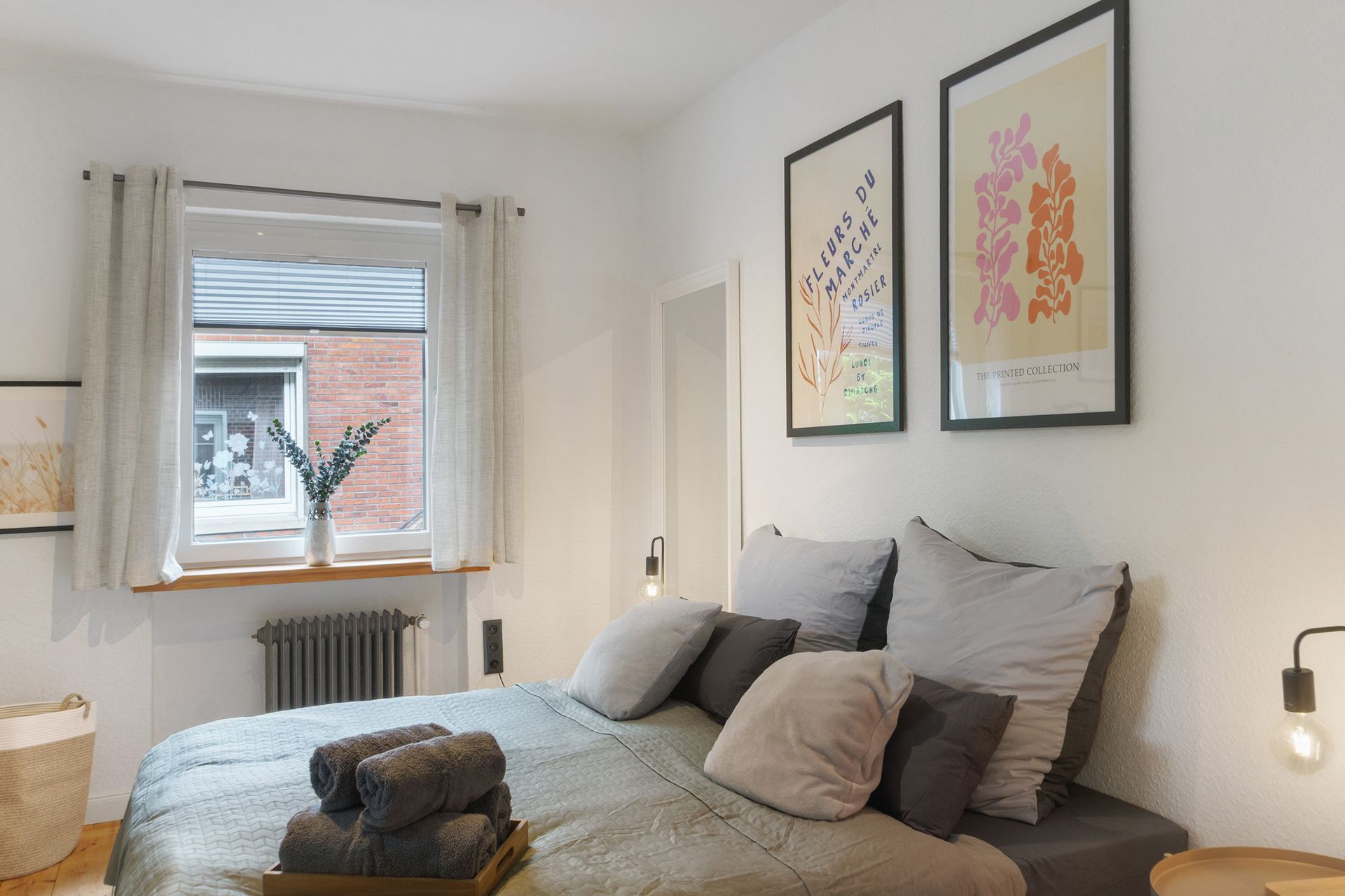 Schlafzimmer mit Bett, Kunstdrucken, Fenster und neutraler Farbpalette.