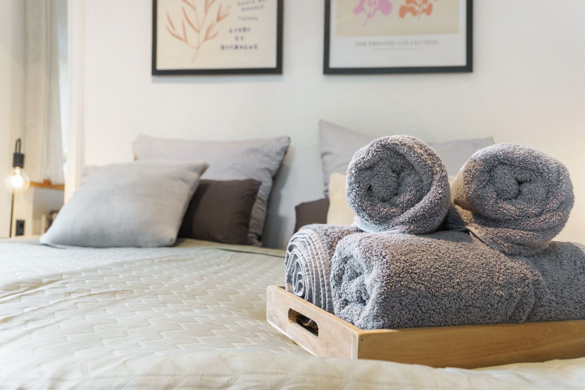 Schlafzimmer mit Bett, Kissen, grauen Handtüchern und gerahmten Bildern.