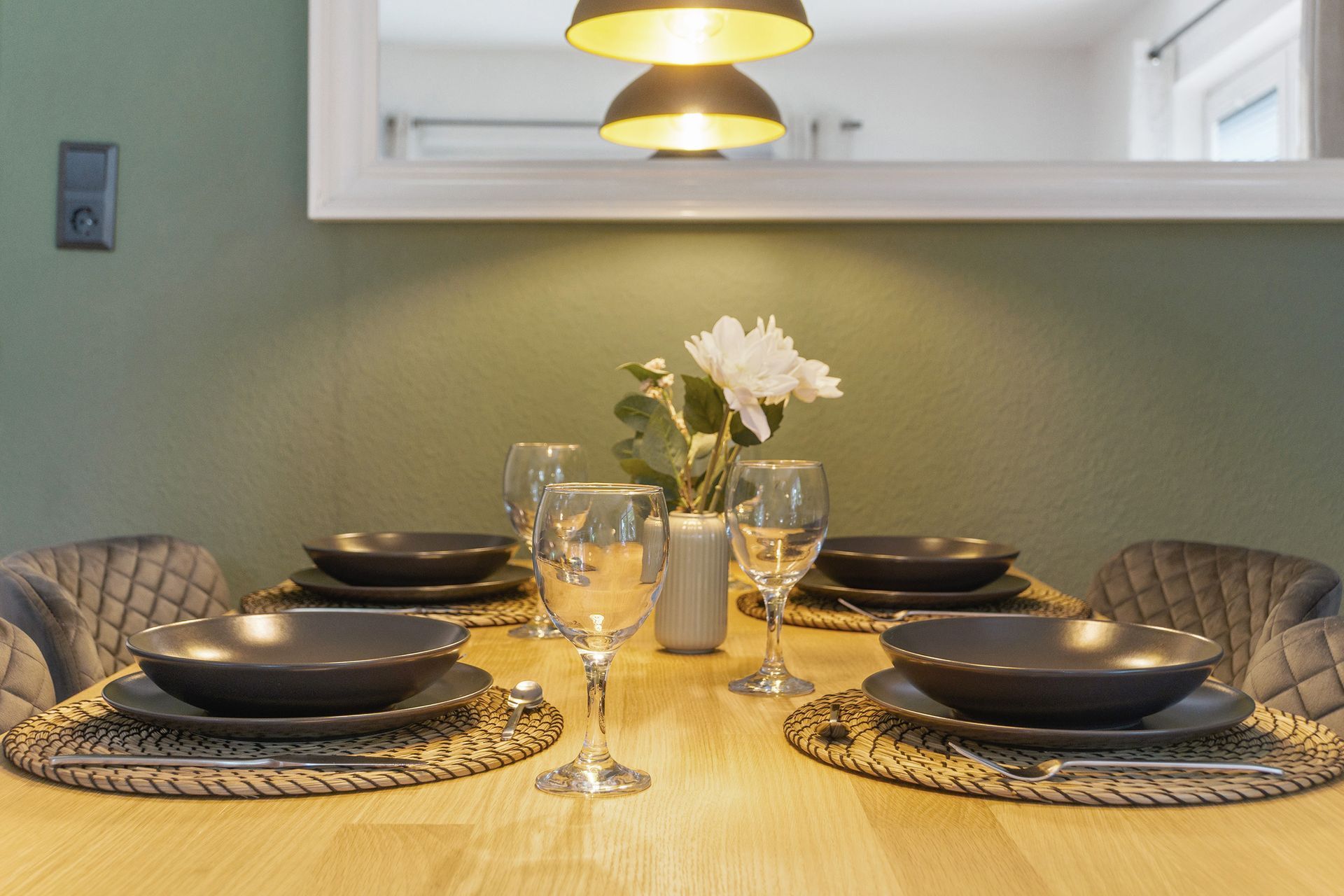 Ein Esstisch für sechs Personen ist mit grauem Geschirr, Blumen und Pendelleuchten gedeckt.