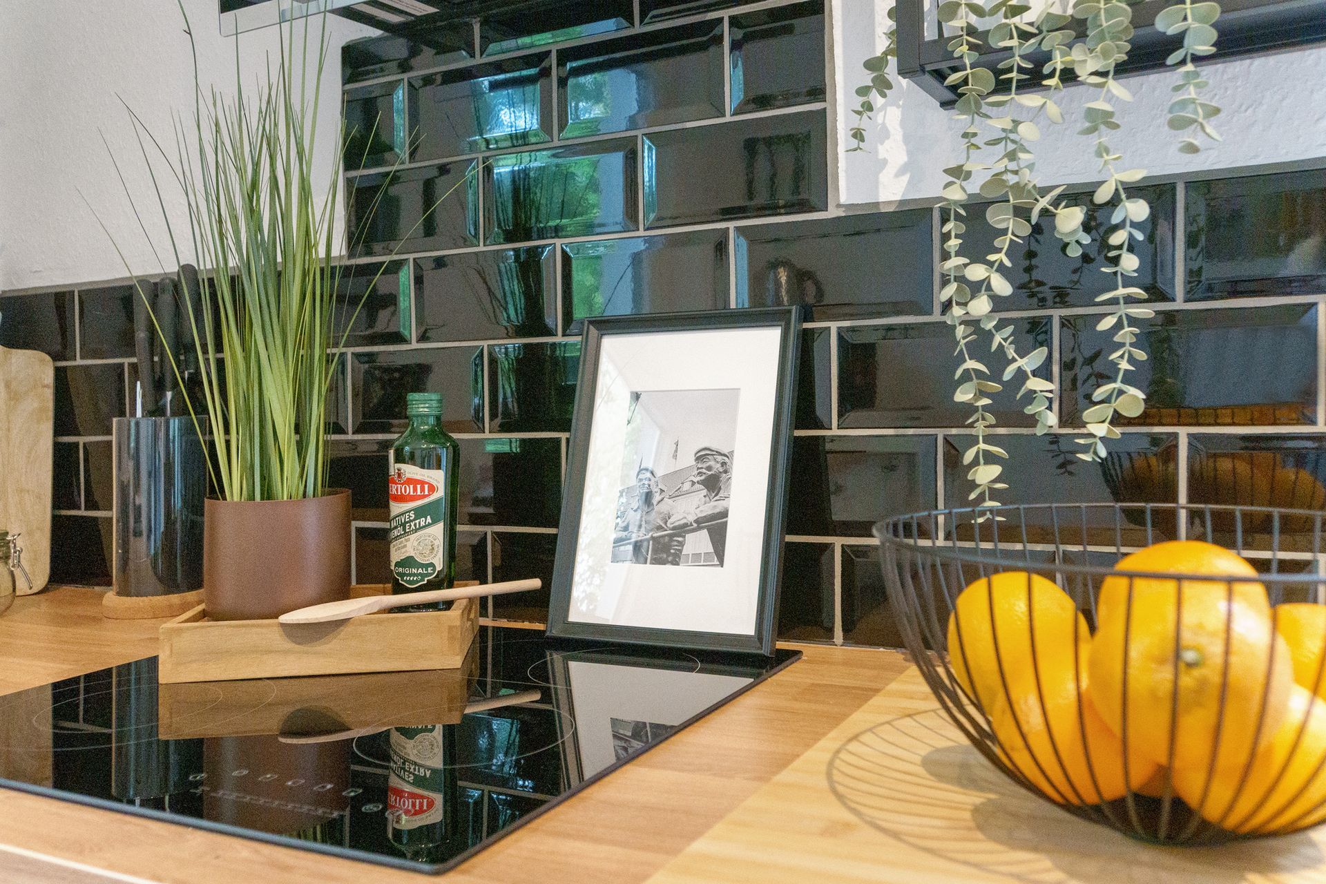 Küchenarbeitsplatte mit schwarzem Spritzschutz, Pflanzen, gerahmtem Foto und einer Schale mit Orangen.