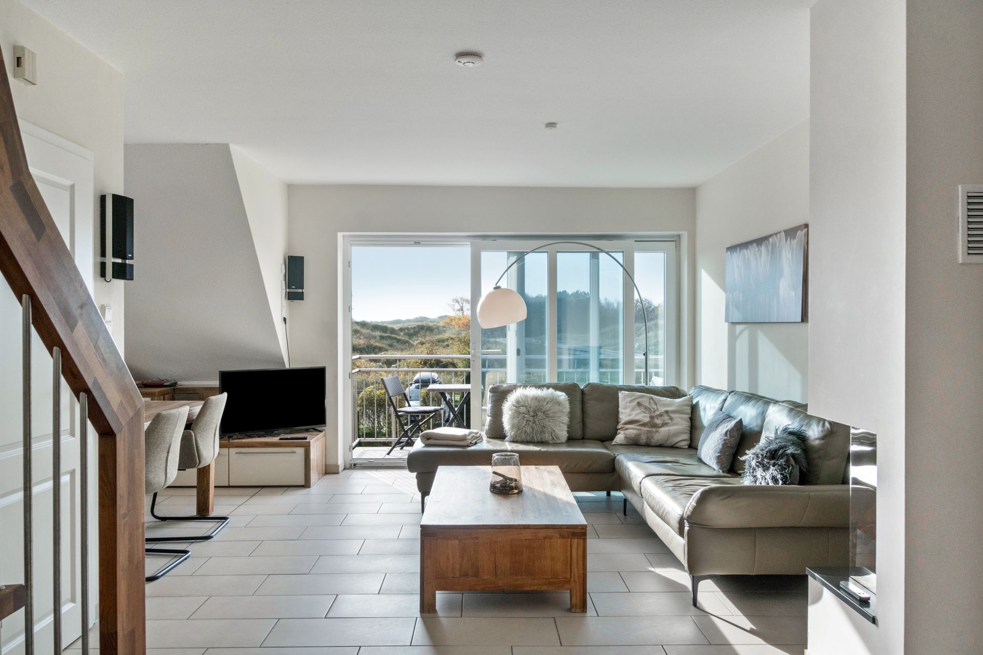 Wohnzimmer mit Ecksofa, Couchtisch aus Holz, Schiebetüren zum Balkon und Treppe.