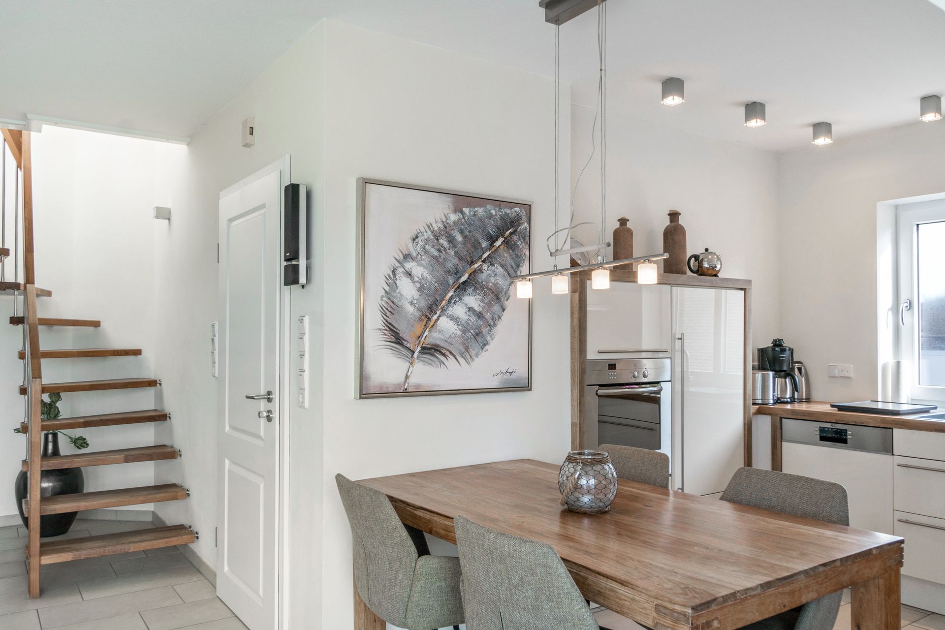 Essbereich mit Holztisch, grauen Stühlen, Kunstwerken und einer Treppe, die nach oben führt.