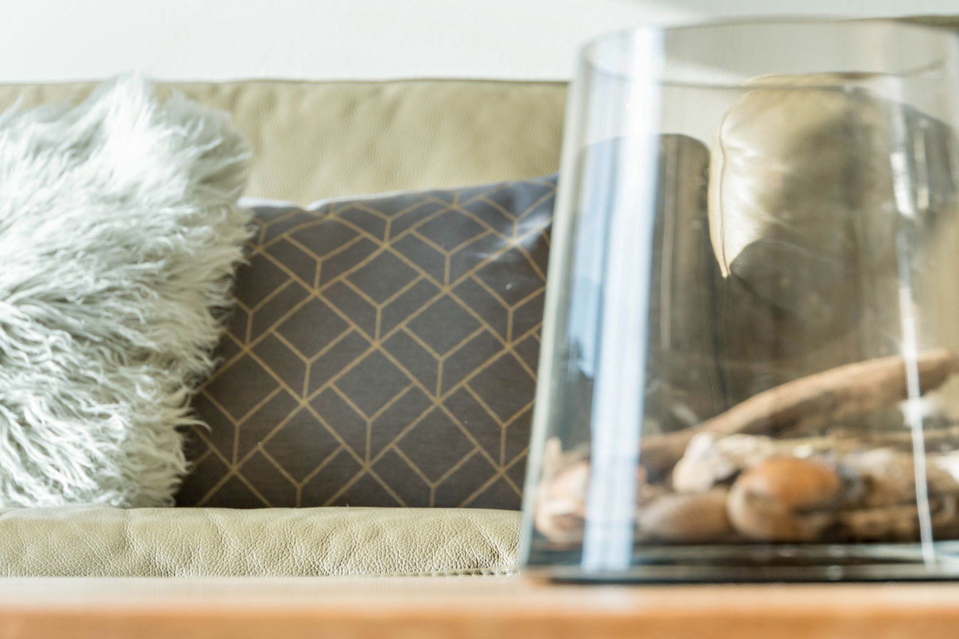Sofa mit Kissen und eine Glasvase auf einem Holztisch. In der Vase befinden sich kleine Kieselsteine.