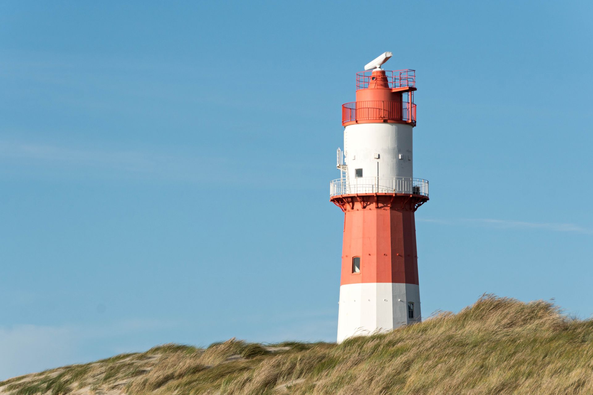 Ein weiß-roter Leuchtturm auf einem sandigen Hügel unter klarem, blauem Himmel.