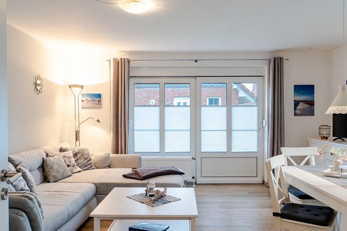 Wohnzimmer mit beigefarbenem Ecksofa, weißem Tisch und Glasschiebetür.