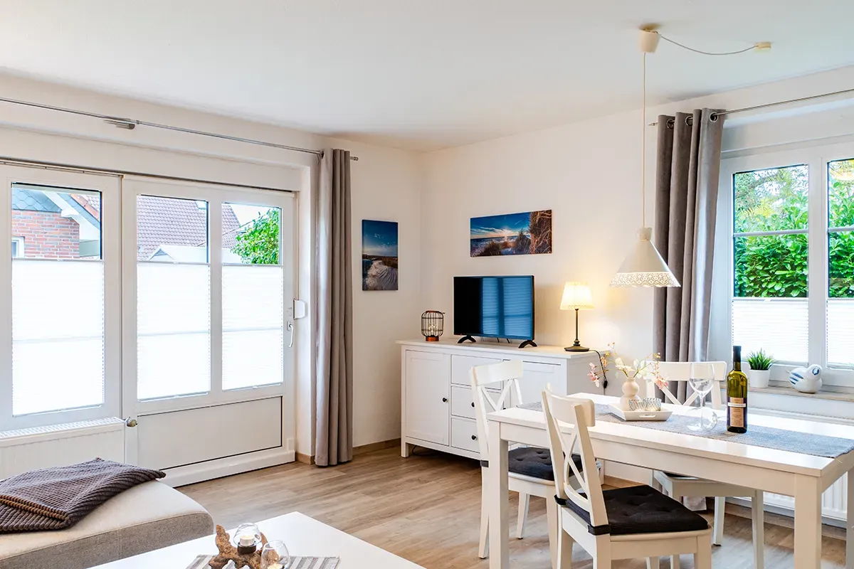 Heller Wohnraum mit weißen Möbeln, Holzböden und großen Fenstern.