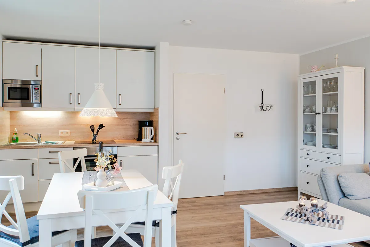 Weiße Küche/Essbereich mit gedecktem Tisch, Schränken und einem Buffetschrank.