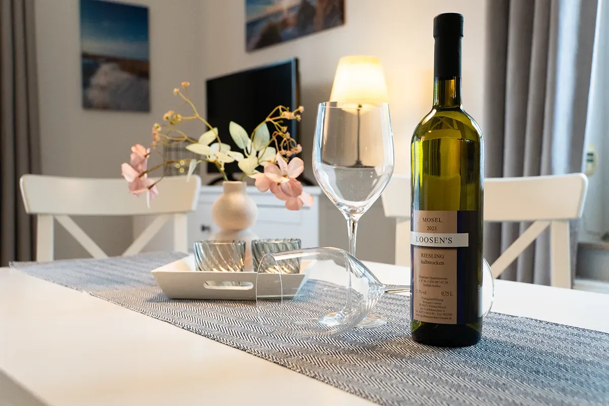 Ein mit einer Weinflasche, Gläsern, Blumen und einem Tablett gedeckter Tisch in einem Zimmer mit Gemälden und einem Fernseher.