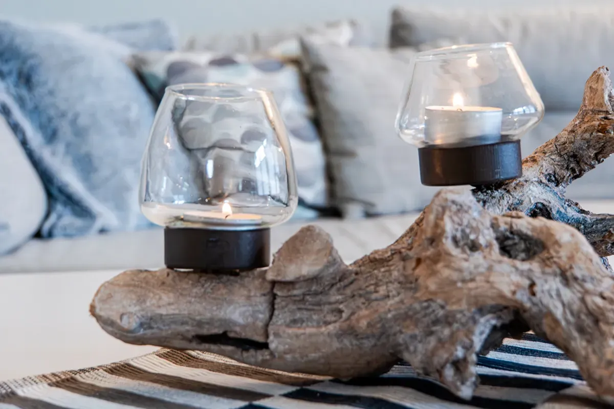 Zwei beleuchtete Kerzenhalter auf Treibholz, im Hintergrund Kissen.