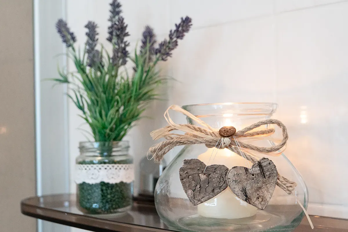 Lavendelzweige in einem Glas neben einer Kerze in einem verzierten Glasgefäß auf einem Regal.