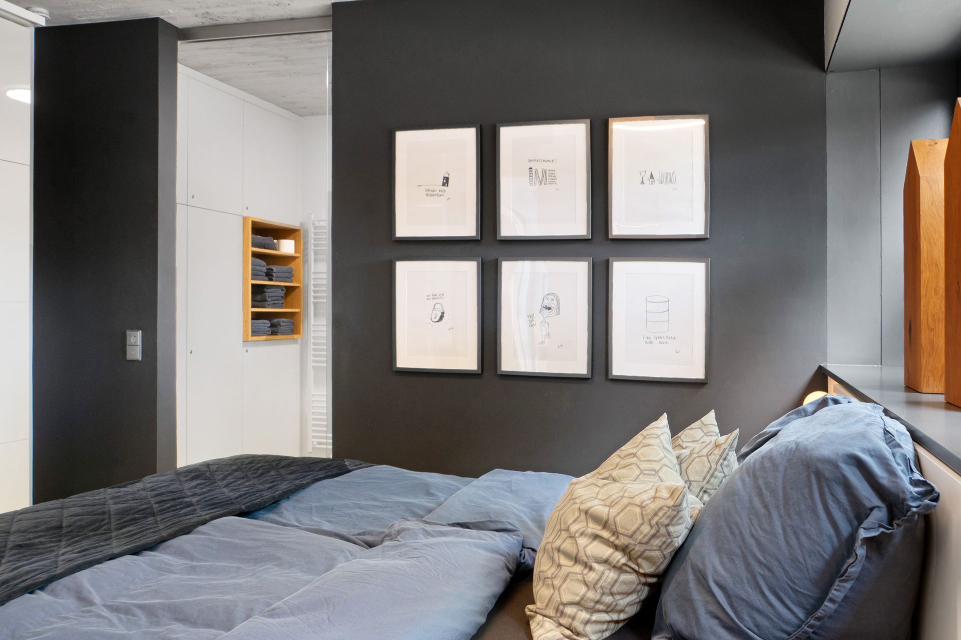 Schlafzimmer mit Bett, dunkelgrauer Wand mit gerahmten Bildern und eingebautem Regal.