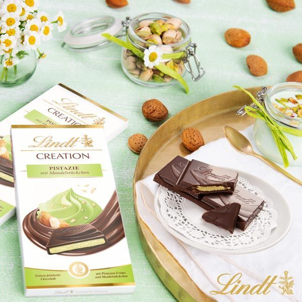 Werbung & Content -Eine Schachtel Lindt Creation Pistazienschokolade steht auf einem Tisch neben einem Teller mit Schokolade.