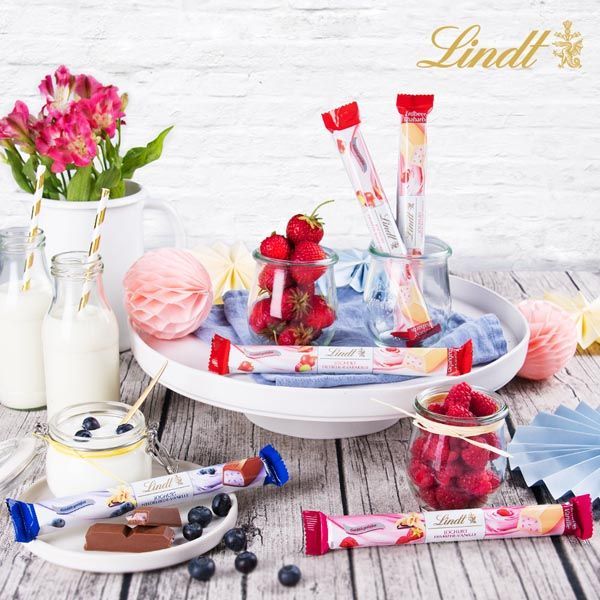 Werbung & Content -Ein Holztisch mit einem Tablett voller Lindt-Pralinen und Erdbeeren.