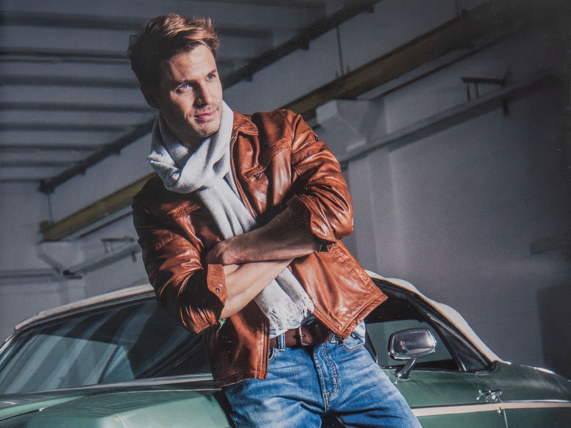 Modefotografie - Ein Mann in einer braunen Lederjacke lehnt an einem grünen Auto.