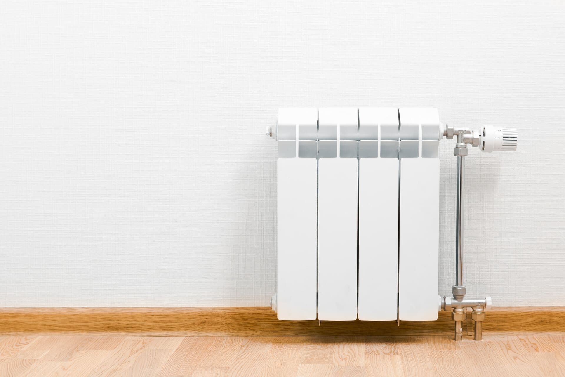 Radiador blanco sobre un piso de madera clara contra una pared blanca texturizada.
