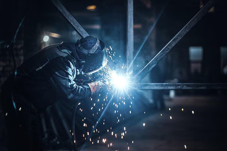 Professioneller Schweißer bei der Arbeit an einem großen Metallkonstrukt, hell leuchtender Lichtbogen