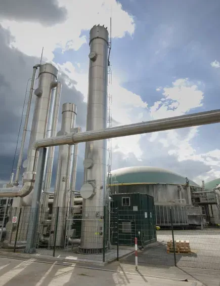 Industrieanlage mit hohen silbernen Schornsteinen, Rohren und einem kuppelförmigen Gebäude unter einem bewölkten Himmel