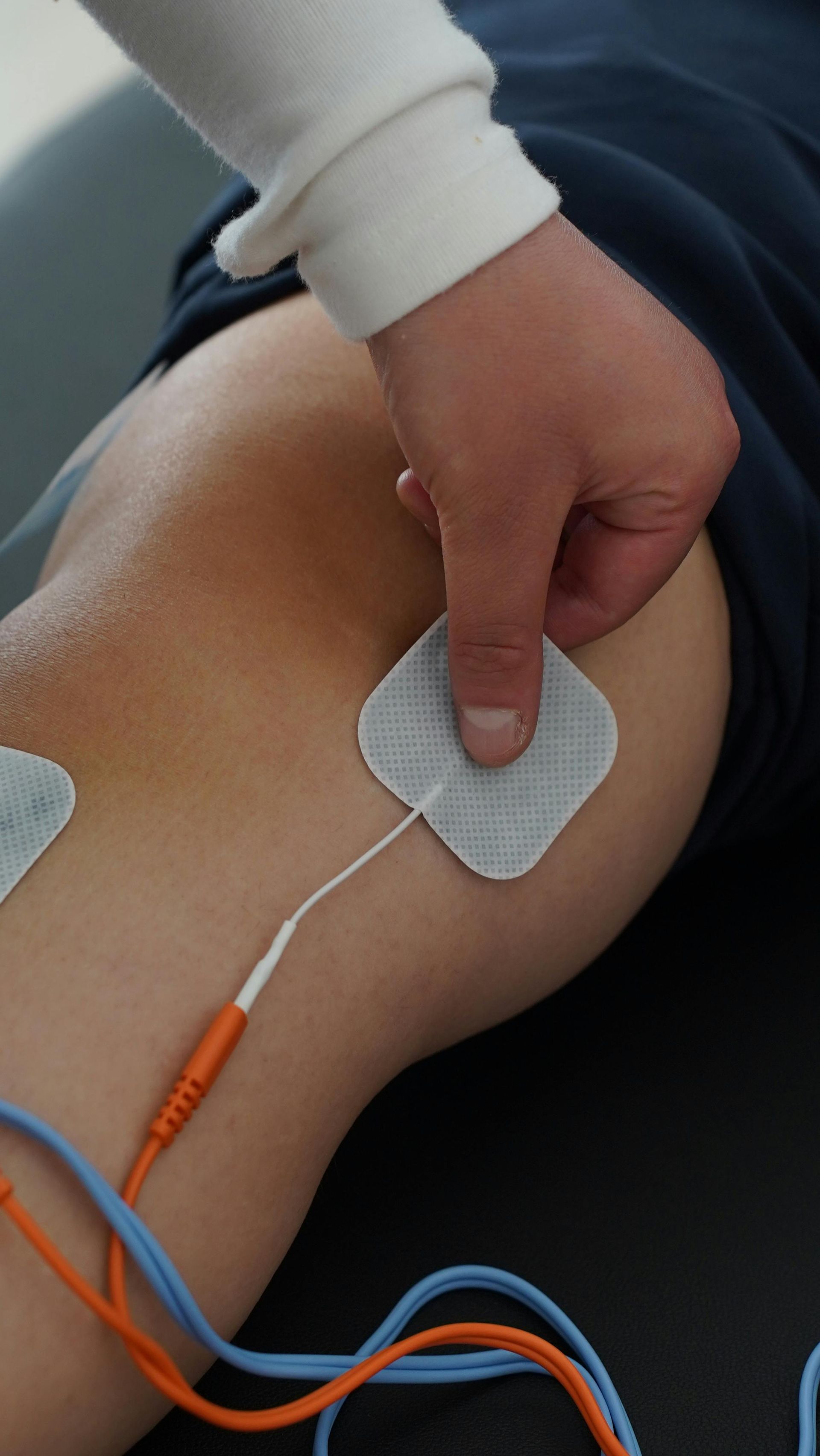 Person, die ein Elektrodenpad zur Elektrotherapiebehandlung am Knie anbringt.