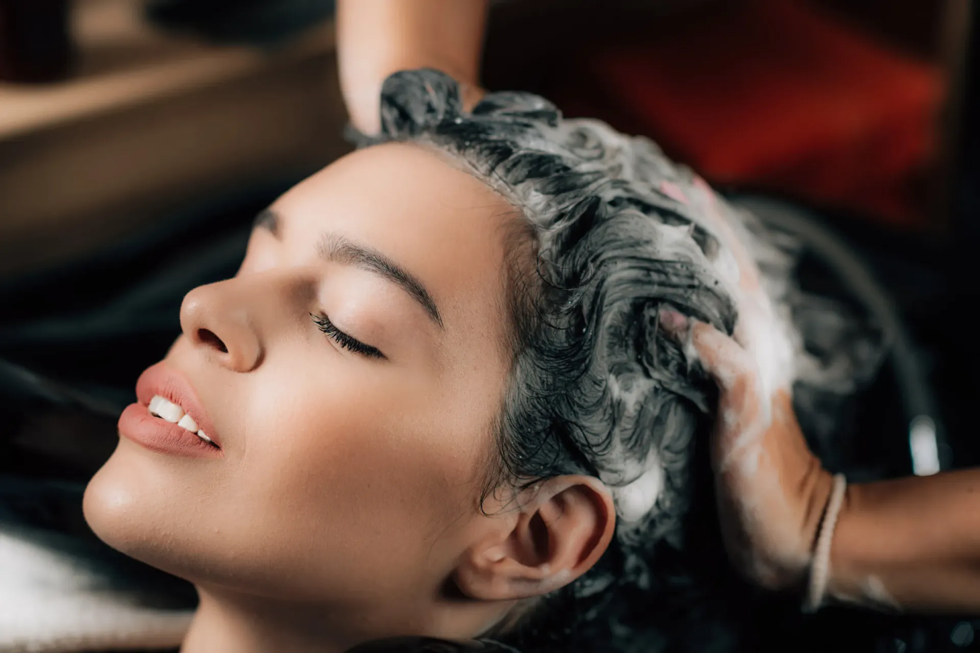 Mujer lavándose el pelo en una peluquería, con los ojos cerrados y enjabonada. Masajeándose las manos.