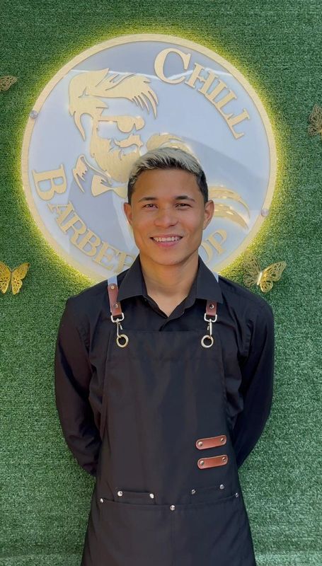 Hombre con delantal negro, de pie frente al cartel de