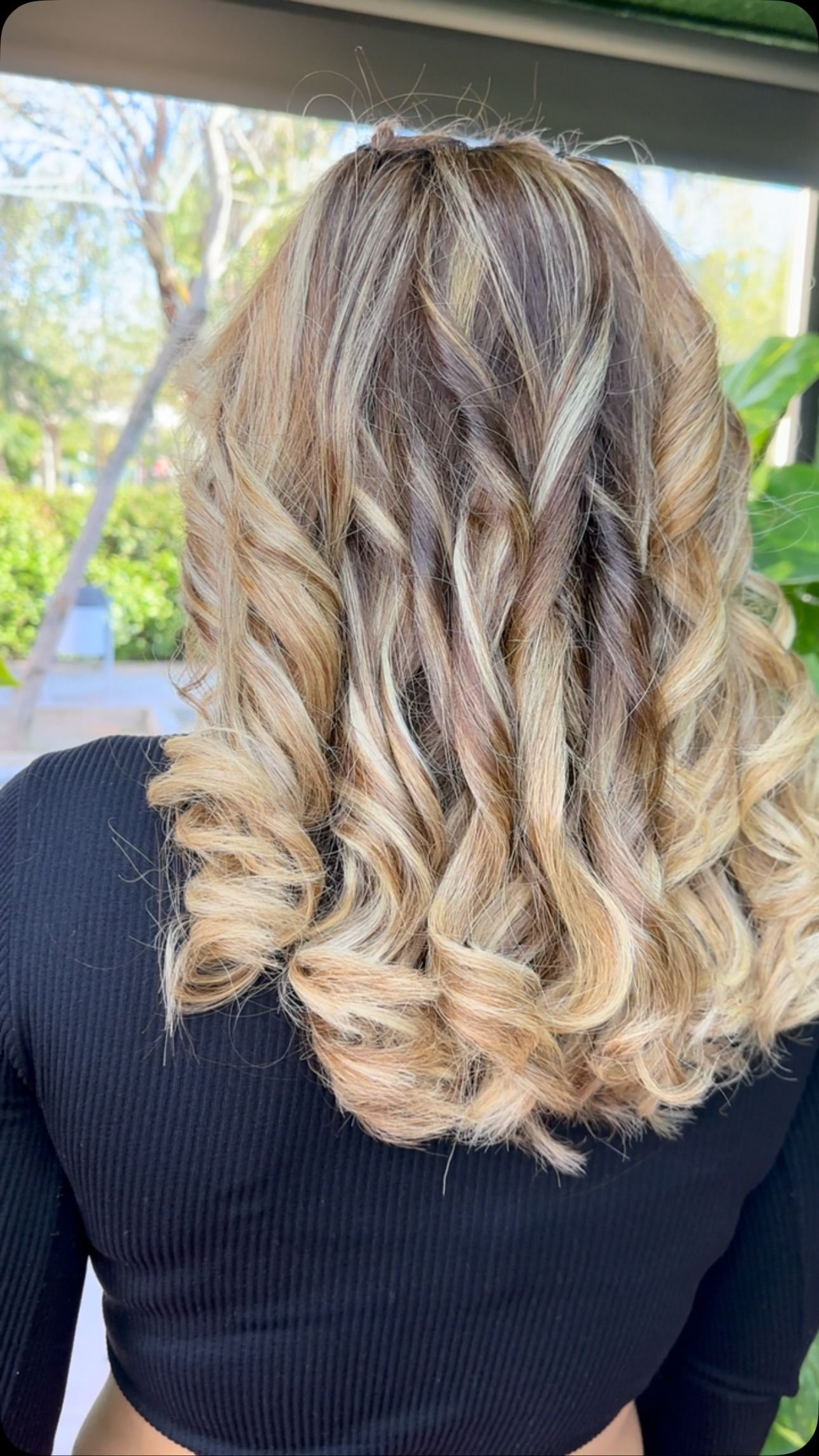 Mujer con cabello rizado, en capas, castaño claro y rubio, con ombré. Top negro.