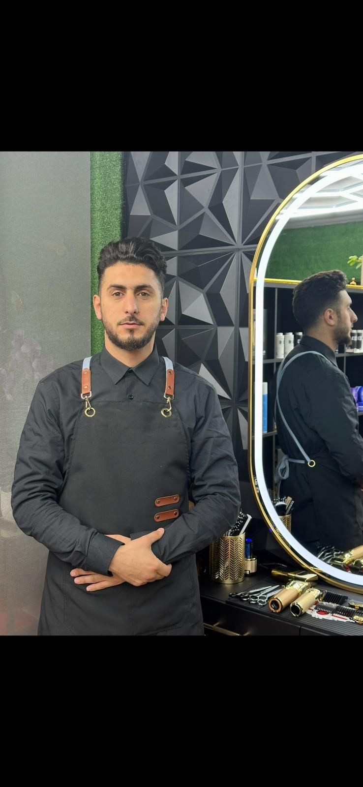 Un barbero con un delantal negro de pie frente a un espejo en una barbería.