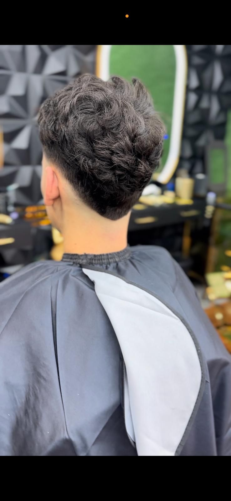 Una persona con un corte de pelo oscuro y texturizado en un salón, vistiendo una capa de barbero.
