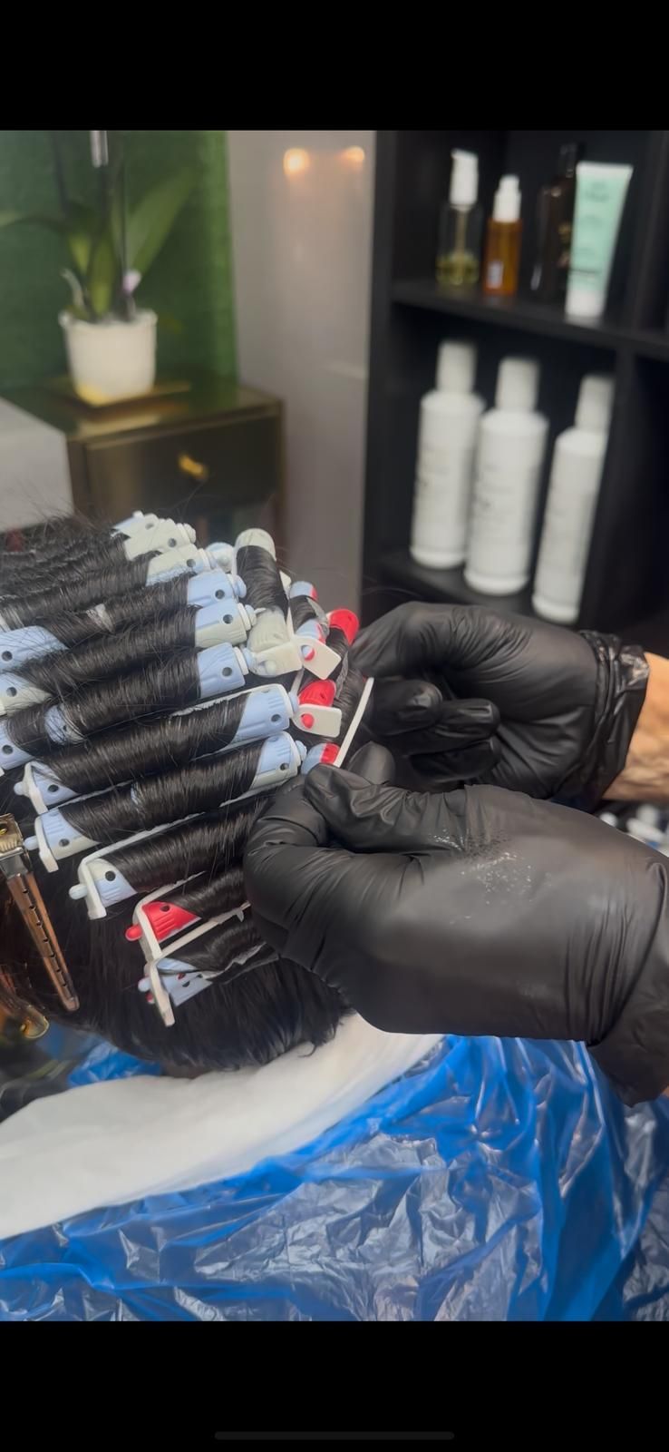 Unas manos enguantadas de negro trabajan con rulos para el cabello, preparando una permanente.
