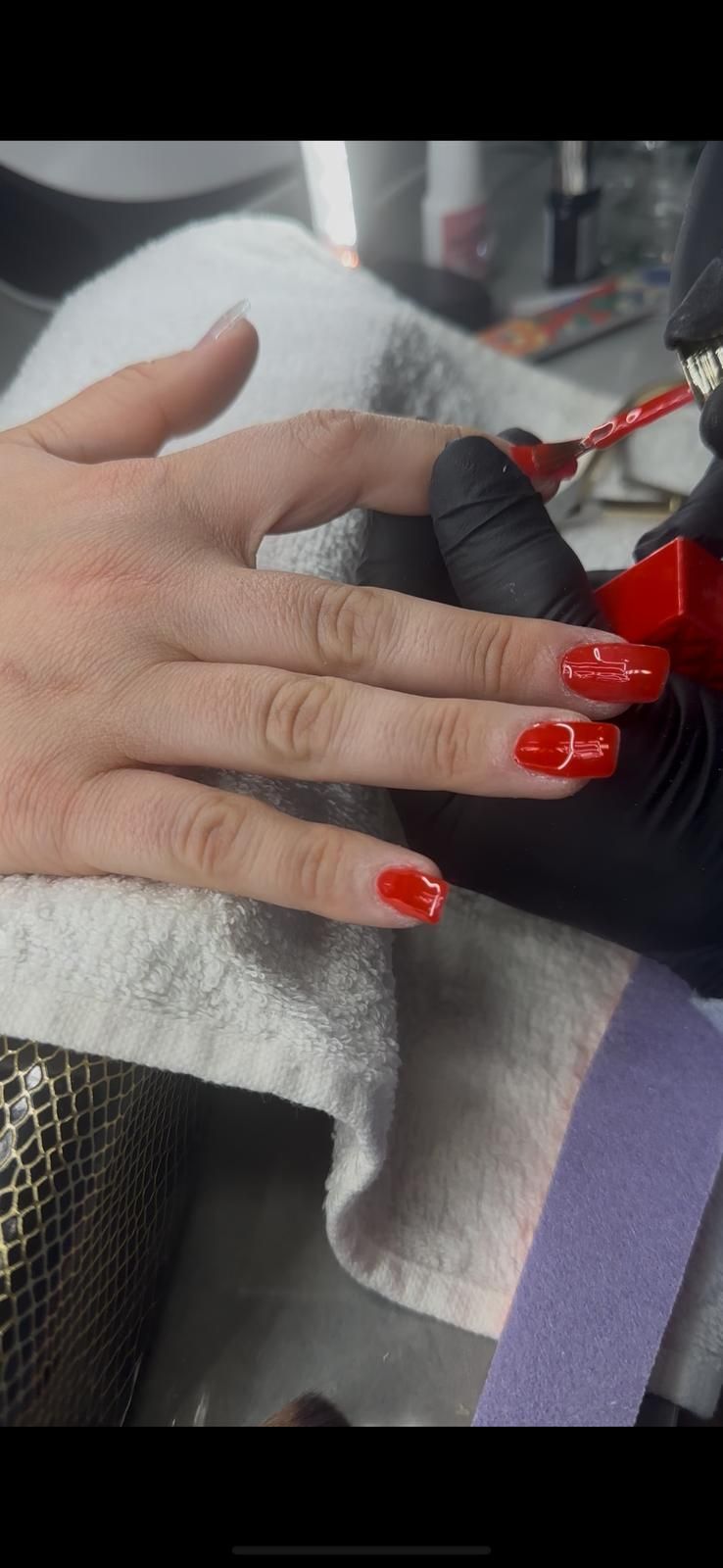 La mano de una persona con esmalte de uñas rojo aplicándose en un salón de uñas.
