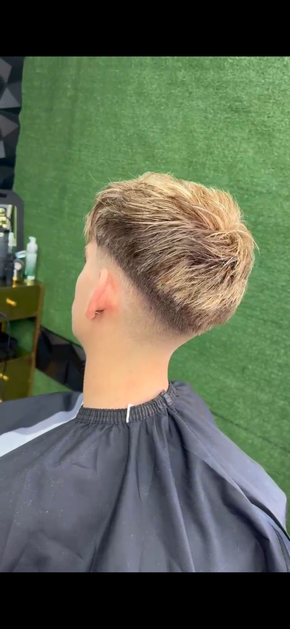 La cabeza de una persona con un corte de pelo descolorido, sobre un fondo verde.