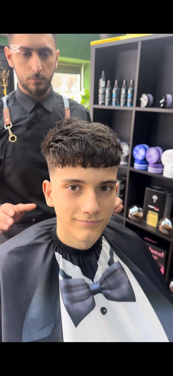 Una persona cortándose el pelo en una barbería. Lleva una capa de barbero.