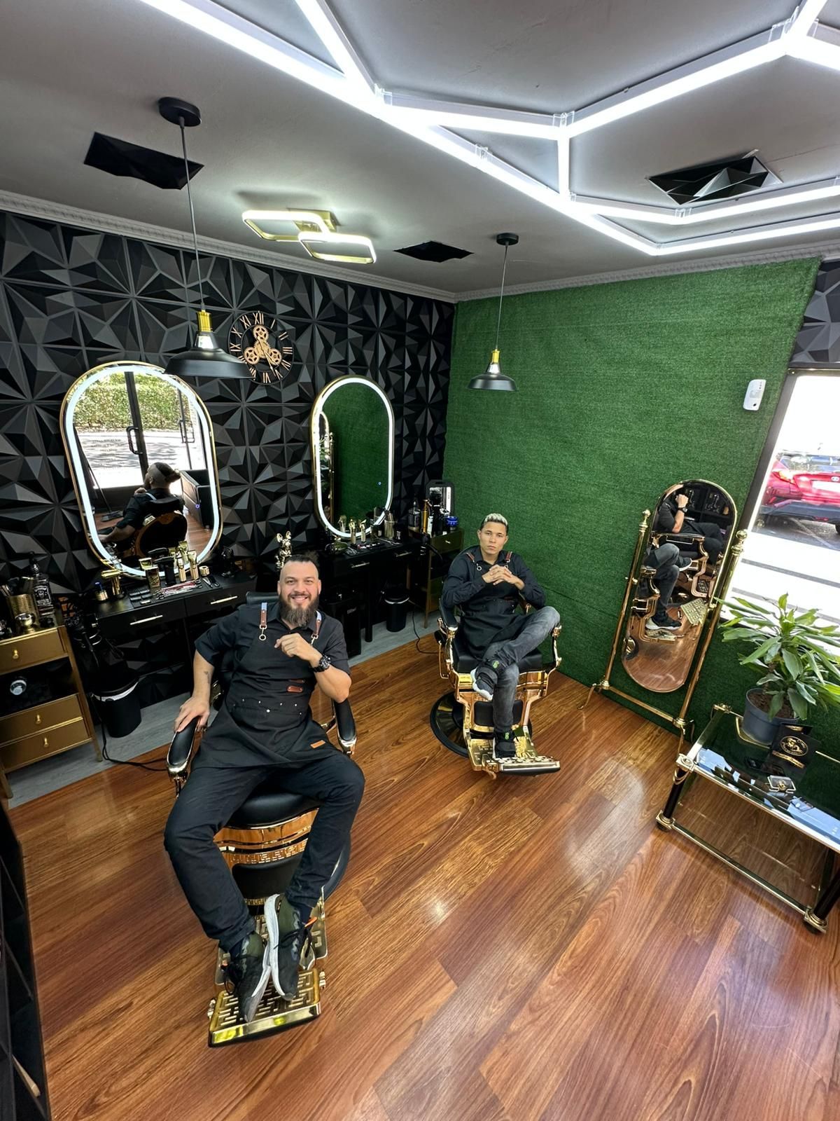 Dos hombres se relajan en una barbería decorada en negro y dorado. Uno señala, el otro se sienta.
