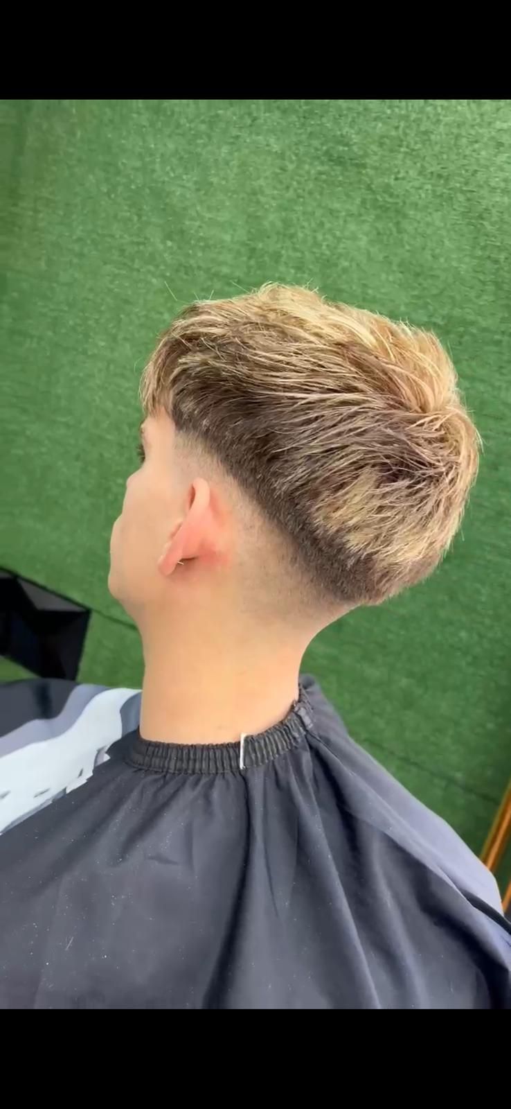 Una persona con un peinado rubio texturizado, que se corta el pelo con los lados descoloridos.